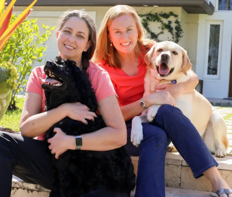 Two individuals happily embracing their pet dogs